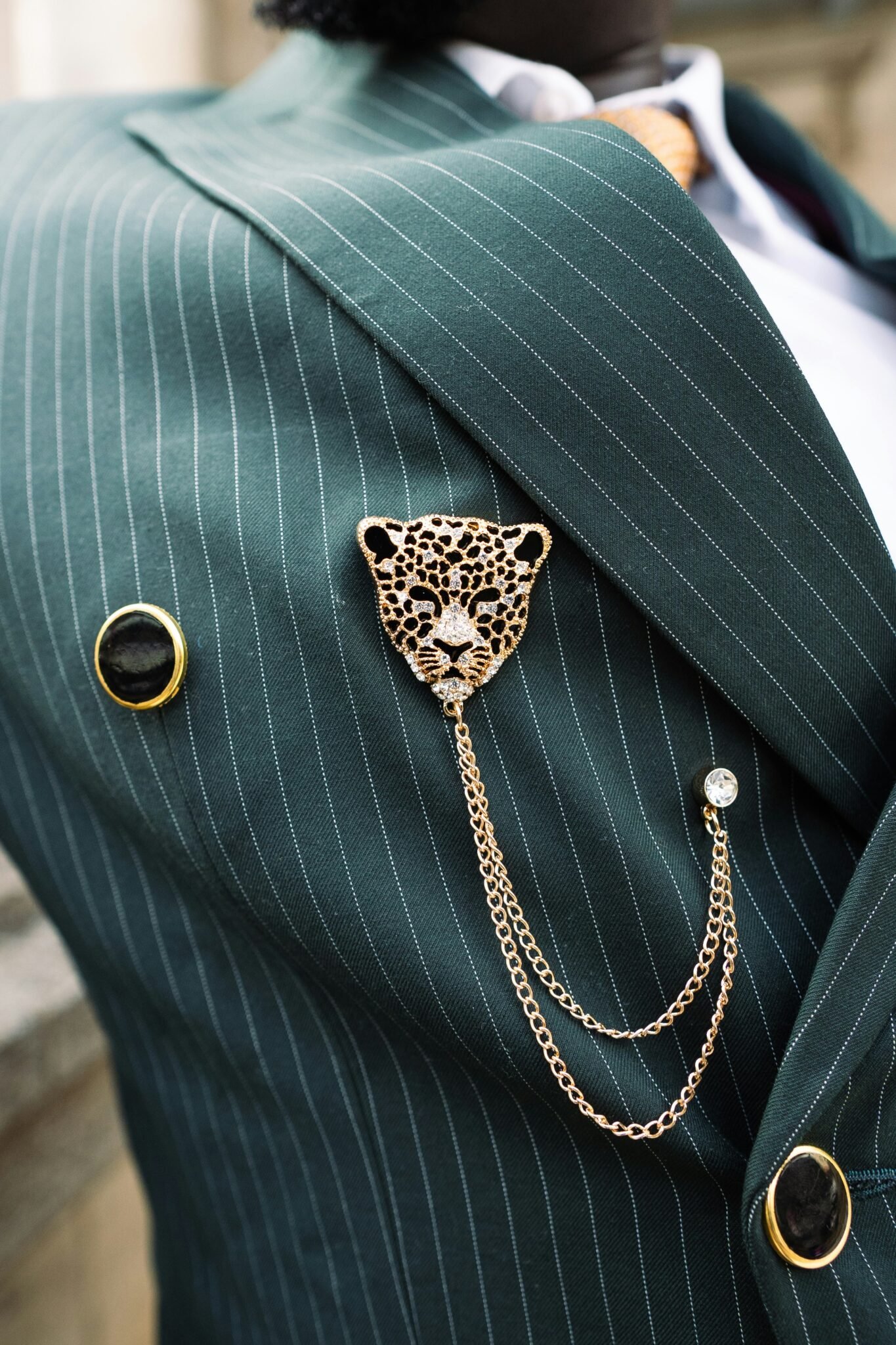 Broche tête de léopard dorée à chaînette sur une veste rayée verte, collection Broches Animaux